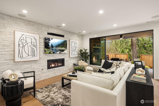 living room with wood-type flooring, a stone fireplace, and ceiling fan