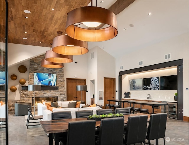 dining area with a high ceiling, wine cooler, wood ceiling, and a fireplace