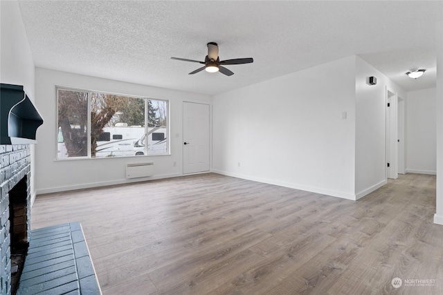 unfurnished living room with ceiling fan, a textured ceiling, a fireplace, and light hardwood / wood-style flooring