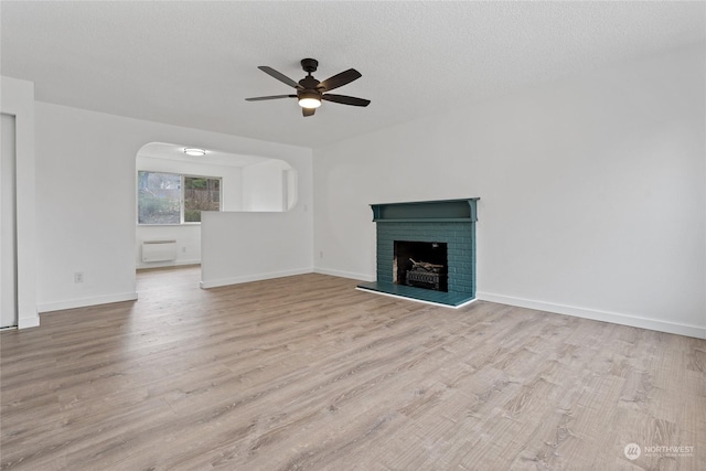 unfurnished living room featuring ceiling fan, a brick fireplace, a textured ceiling, and light wood-type flooring