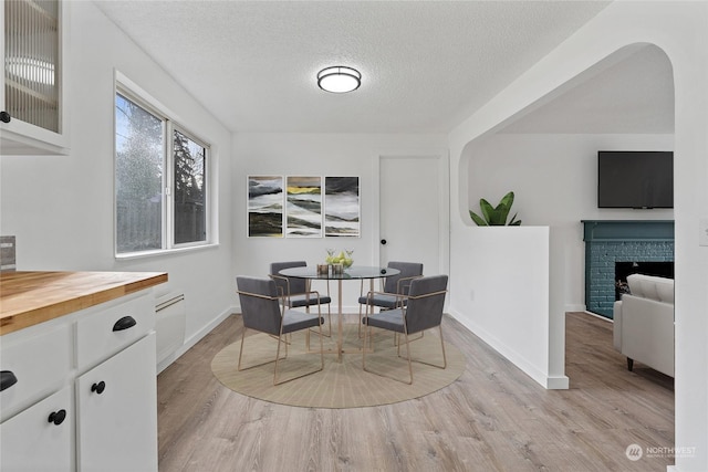 dining area with a brick fireplace, light hardwood / wood-style flooring, and a textured ceiling