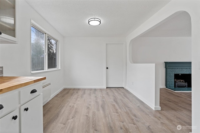 unfurnished dining area with a brick fireplace, a textured ceiling, and light wood-type flooring