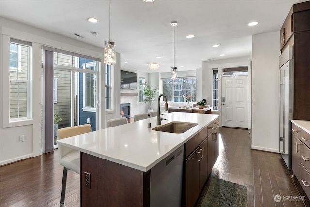 kitchen with appliances with stainless steel finishes, decorative light fixtures, sink, dark brown cabinets, and a center island with sink