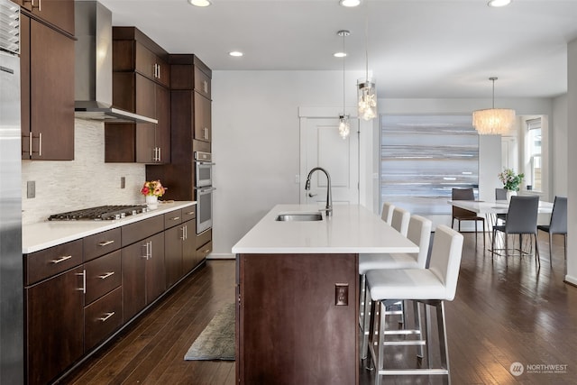 kitchen featuring appliances with stainless steel finishes, decorative light fixtures, sink, a kitchen bar, and wall chimney range hood