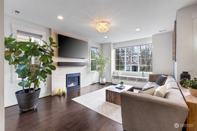 living room with dark wood-type flooring, a large fireplace, and a healthy amount of sunlight