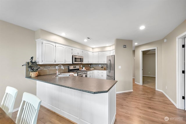 kitchen featuring appliances with stainless steel finishes, white cabinetry, sink, decorative backsplash, and kitchen peninsula