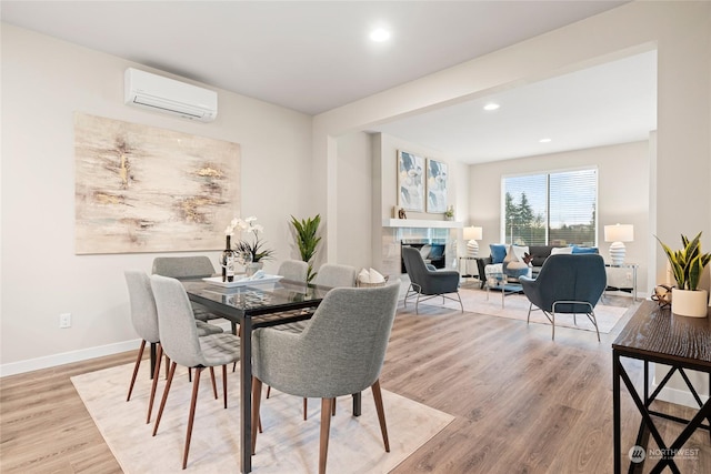 dining room featuring a wall mounted AC, a tile fireplace, and light hardwood / wood-style flooring