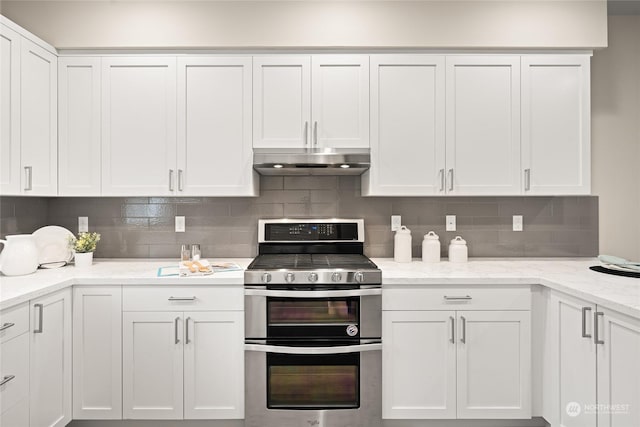 kitchen featuring tasteful backsplash, light stone counters, range with two ovens, and white cabinets