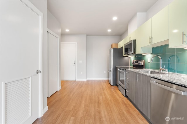 kitchen featuring stainless steel appliances, sink, light wood-type flooring, and decorative backsplash