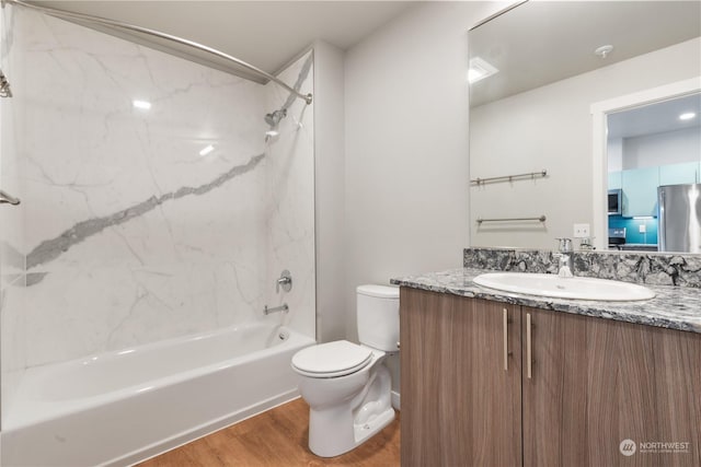 full bathroom with hardwood / wood-style flooring, tiled shower / bath, vanity, and toilet