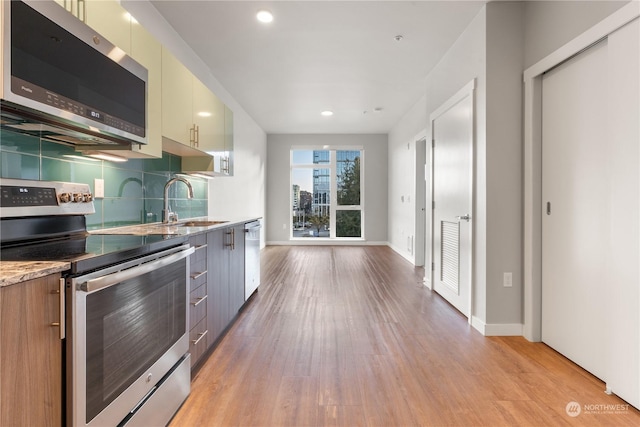 kitchen with sink, light hardwood / wood-style flooring, stainless steel appliances, decorative backsplash, and cream cabinetry