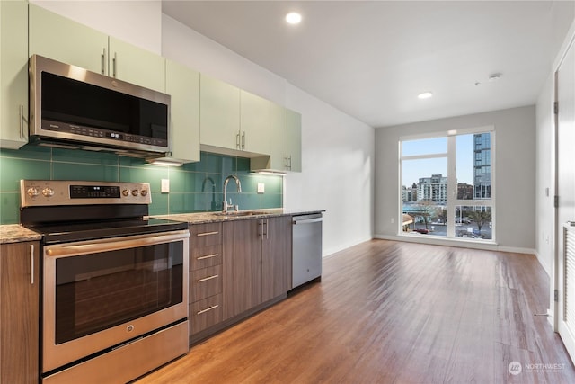 kitchen with sink, tasteful backsplash, light hardwood / wood-style flooring, appliances with stainless steel finishes, and green cabinets