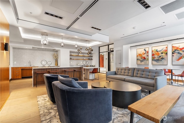 living room featuring a raised ceiling, sink, and light wood-type flooring