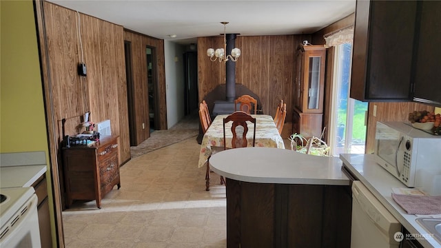 kitchen with a wood stove, pendant lighting, white appliances, and wood walls