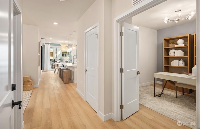 hallway with an inviting chandelier and light wood-type flooring