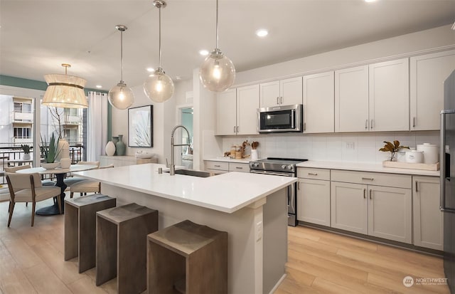 kitchen featuring sink, decorative light fixtures, stainless steel appliances, a kitchen island with sink, and backsplash