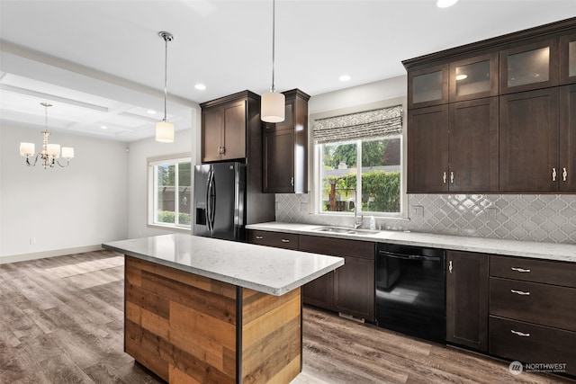 kitchen featuring sink, hanging light fixtures, a center island, light stone counters, and black appliances