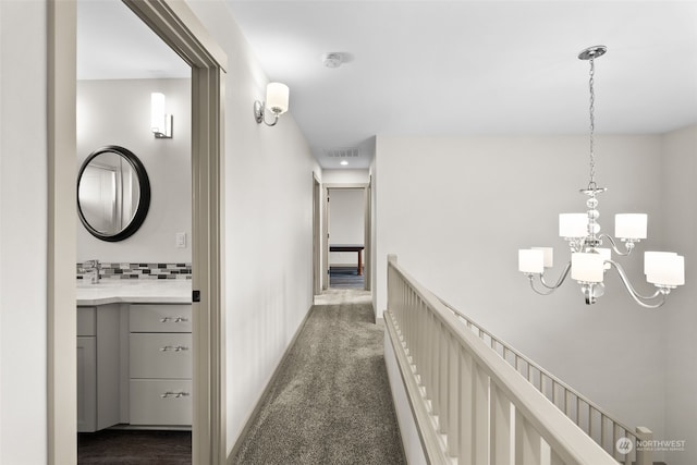 corridor featuring a notable chandelier and dark colored carpet