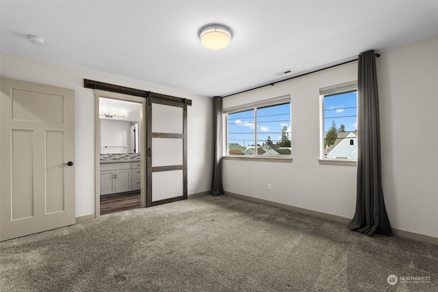 unfurnished bedroom with carpet flooring, connected bathroom, and a barn door