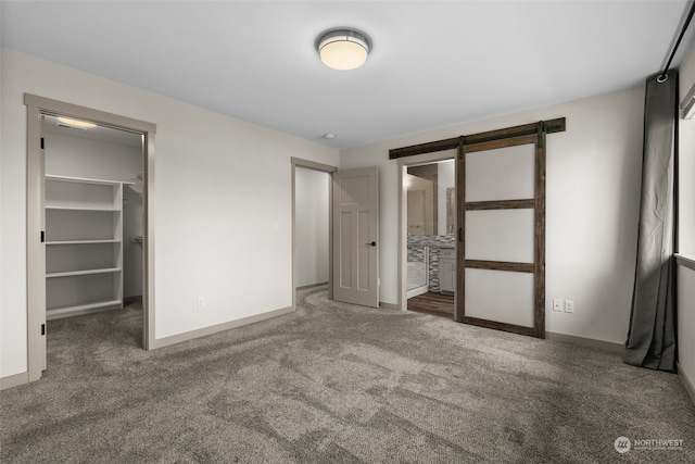 unfurnished bedroom featuring dark carpet, a spacious closet, ensuite bath, and a barn door