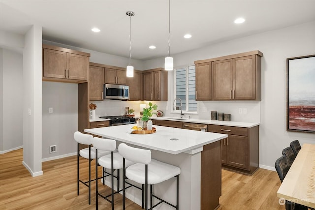 kitchen featuring sink, light hardwood / wood-style flooring, stainless steel appliances, a kitchen island, and decorative light fixtures