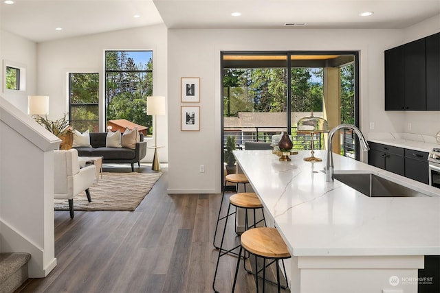 kitchen featuring dark wood-type flooring, an island with sink, a kitchen bar, and sink