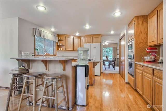 kitchen featuring sink, a kitchen bar, stainless steel appliances, light stone countertops, and light wood-type flooring