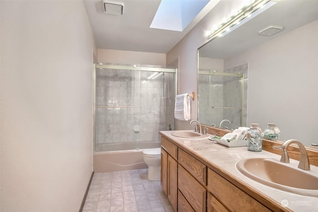 full bathroom featuring a skylight, shower / bath combination with glass door, vanity, toilet, and tile patterned floors