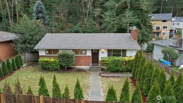 ranch-style house featuring brick siding, a shingled roof, a front lawn, fence, and a chimney