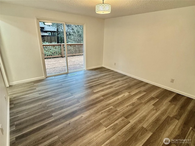 spare room with a textured ceiling, dark wood-type flooring, and baseboards