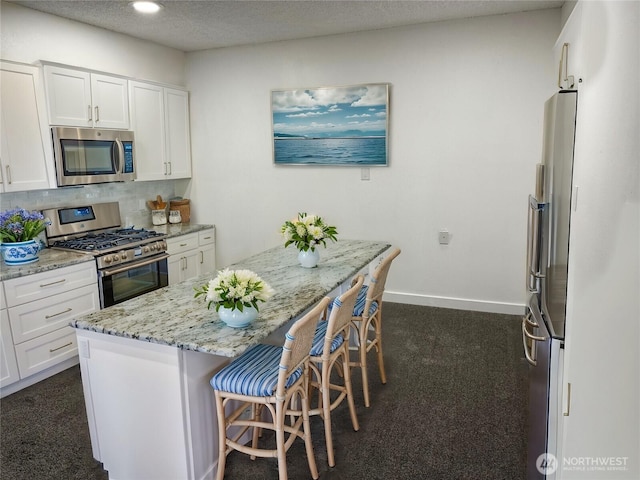 kitchen featuring light stone countertops, white cabinets, appliances with stainless steel finishes, decorative backsplash, and a kitchen bar