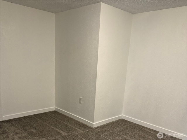 spare room with a textured ceiling, dark carpet, and baseboards