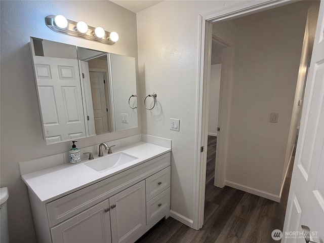 bathroom with toilet, wood finished floors, vanity, and baseboards