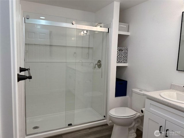 bathroom with toilet, a stall shower, wood finished floors, and vanity