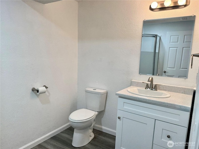 full bath with a stall shower, baseboards, toilet, wood finished floors, and vanity