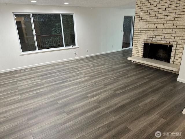 unfurnished living room featuring a textured ceiling, recessed lighting, wood finished floors, baseboards, and a brick fireplace