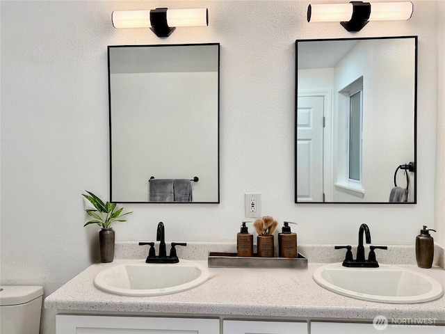 bathroom featuring toilet, double vanity, and a sink