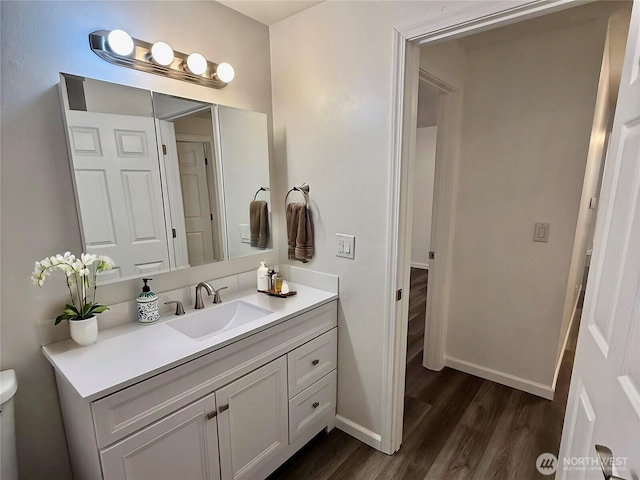 bathroom with toilet, wood finished floors, vanity, and baseboards