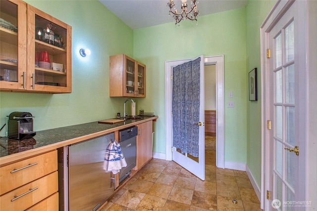 kitchen with dark countertops, glass insert cabinets, baseboards, dishwasher, and an inviting chandelier