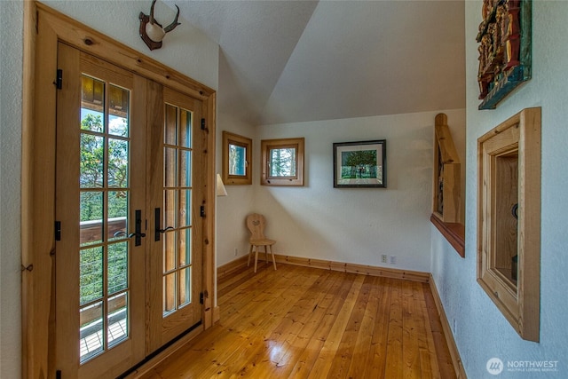 doorway to outside featuring french doors, baseboards, light wood-style floors, and vaulted ceiling