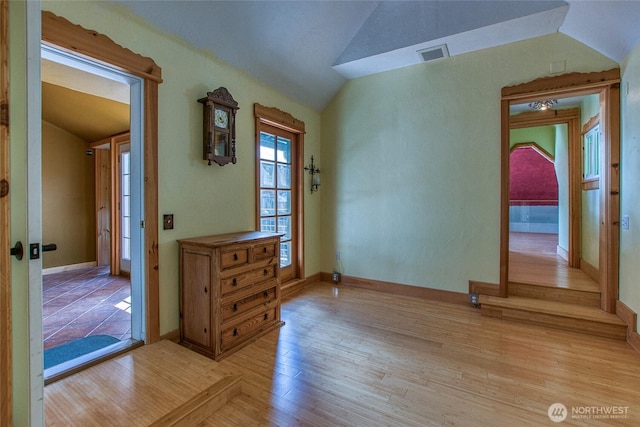 unfurnished room with light wood-type flooring, visible vents, lofted ceiling, and baseboards