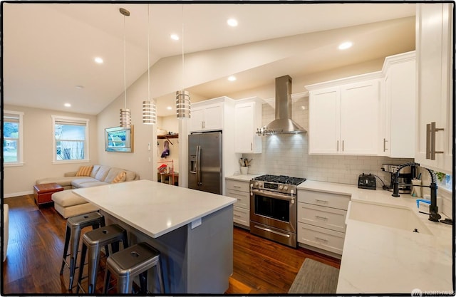 kitchen with hanging light fixtures, wall chimney range hood, a kitchen breakfast bar, stainless steel appliances, and white cabinets