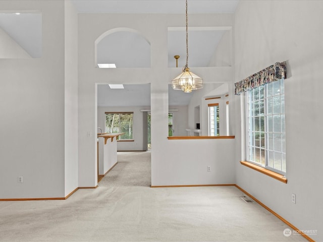 empty room featuring an inviting chandelier, high vaulted ceiling, and light carpet