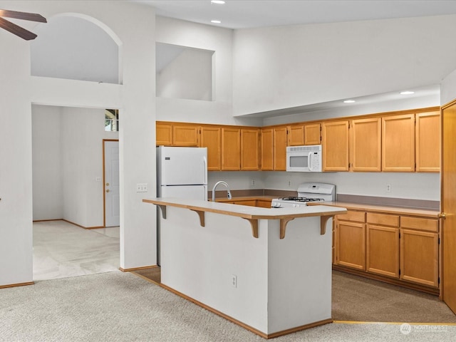 kitchen with high vaulted ceiling, a kitchen bar, light colored carpet, a center island with sink, and white appliances