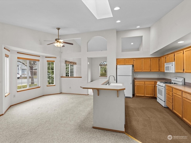 kitchen featuring sink, a skylight, carpet floors, an island with sink, and white appliances