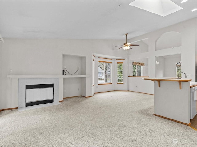 unfurnished living room with a tiled fireplace, light carpet, lofted ceiling with skylight, and ceiling fan