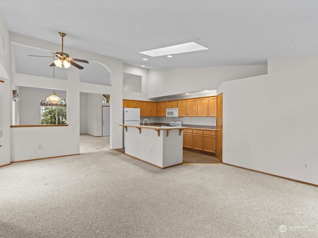 kitchen with a breakfast bar, white appliances, a skylight, light carpet, and ceiling fan