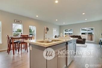 kitchen with sink, an island with sink, dishwasher, and light wood-type flooring