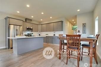 kitchen with light wood-type flooring, a kitchen island, gray cabinets, and appliances with stainless steel finishes