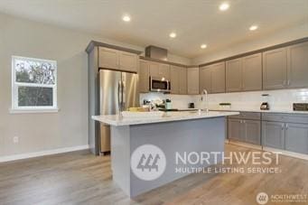 kitchen featuring stainless steel appliances, an island with sink, and gray cabinetry